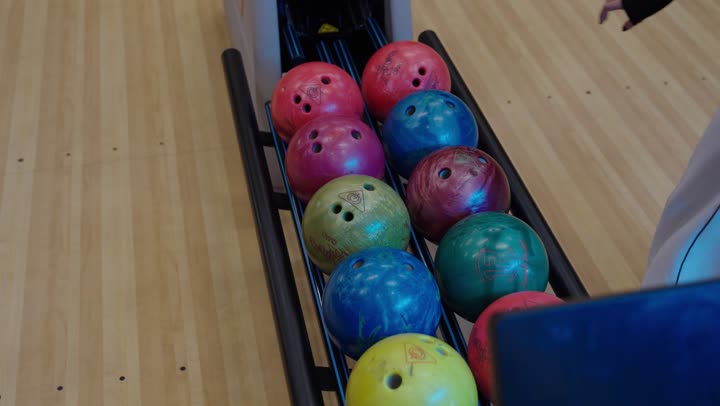 مجموعة من كرات البولينغ الملونة مصفوفة استعدادًا لللعب ,قيام كل فرد من الفريق باختيار كرة خاصة لبداية المنافسة ,مفهوم التنافس والنظام , نشاط ترفيهي عائلي في صالة البولينج