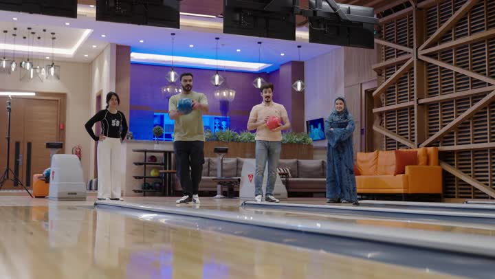 أسرة عربية خليجية سعودية تلعب رياضة البولينع في جو عائلي ودود ,الابنة تشاهد  والدها اثناء رمي الكرة و تقوم بالتهليل لحظة الفوز ,الام تتابع ابنها بشغف وتصفق له بحرارة اثناء تحقيق الفوز , نشاط ترفيهي عائلي في صالة البولينج