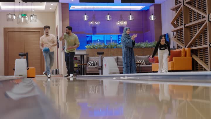عائلة عربية خليجية سعودية تلعب البولينغ في اجواء دافئة ,الام تشجع الابنة بحماس وسعادة ,الاب يشجع الابن بفرحة ,مفهوم العائلة المترابطة ,التنافس والعزيمة في تحقيق الفوز مع حضور الروح الرياضية , نشاط ترفيهي للعائلة في صالة البولينج