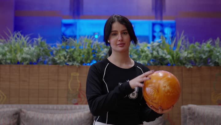 الاصرار على تحقيق الفوز ,فتاة عربية ترتدي الزي الكاجوال تمسك كرة بولينغ صفراء اللون باحترافية عالية , ابتسامة الثقة في الفوز ,نشاط ترفيهي للعائلة فى صالة البولينج