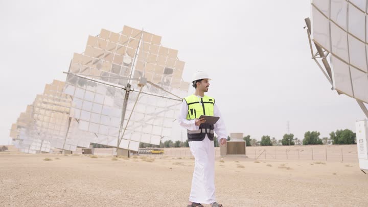 استخدام جهازالتابلت, مهندس عربي خليجي عمانى يشرف على محطات الطاقة الشمسية في السعودية، إرتداء خوذة وسترة الحماية الخاصة بالعمل، مخططات وتصاميم هندسية، محطات الطاقة الشمسية المتجددة، الواح وستلايت انتاج الطاقة الكهربائية