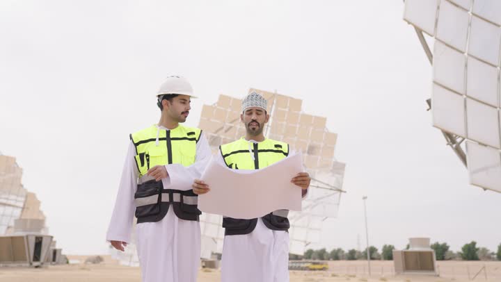 تبادل الخبرة و الرأى بين الزملاء,  مهندسان عربيان خليجيان عمانيان يشرفان على محطات الطاقة الشمسية يحملان مخطط و تصميم هندسى، إرتداء خوذة وسترة الحماية,  الإشراف على العمل، ستلايت، أنظمة الطاقة الشمسية