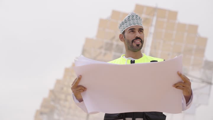 Looking at something, studying the basics of the project, a rear view of an Arab Gulf Omani engineer wearing a dishdasha, kumma, and safety vest, professions and jobs for youth in the Sultanate of Oman, auditing and reviewing engineering plans.
