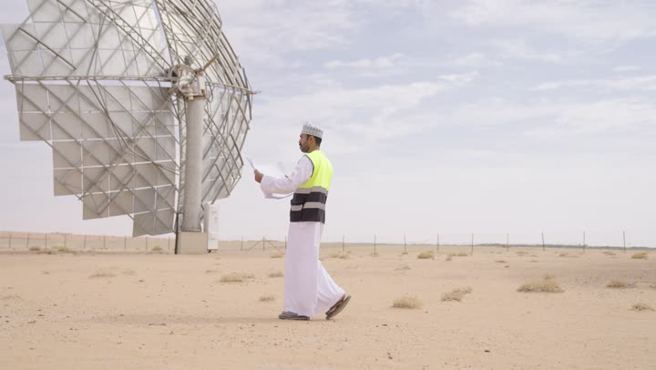 تقدم وتطور سلطنة عمان على يد أبناء الوطن, الاهتمام بشؤون العمل, مهندس عربي خليجي عماني يرتدي الدشداشة والكمة و سترة الحماية ينظر بإيماءات السرور  يحمل بيده مخططات وتصاميم هندسية, التدقيق والإشراف على العمل