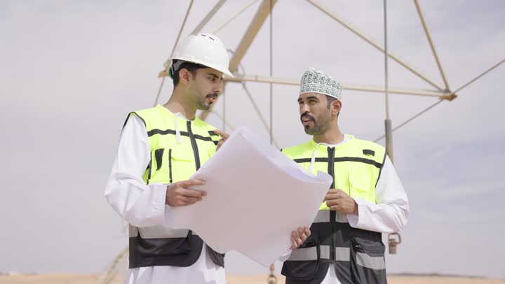 مفهوم دراسة المخطط والمشروع الهندسى, مهندسان عربيان خليجيان عمانيان يشرفان على محطات الطاقة الشمسية ، إرتداء خوذة وسترة الحماية ، الإشراف على العمل، ستلايت، أنظمة الطاقة الشمسية,  تبادل الخبرة و الرأى