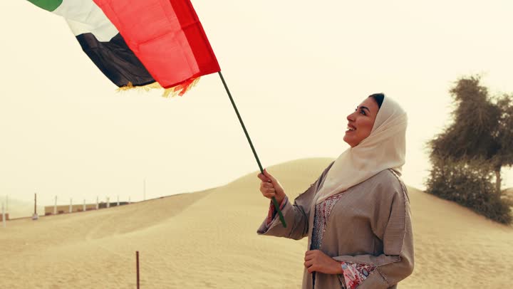 تعابير وايماءات الفخر والاعتزاز، يوم العلم 3 نوفمبر, لامراة عربية خليجية اماراتية ترتدي العباءة والحجاب ترفع علم الإمارات في الصحراء, مفهوم حب الوطن والانتماء اليه, إحياء ذكرى استقلال دولة الإمارات العربية المتحدة, ذكرى تأسيس الاتحاد 2 ديسمبر