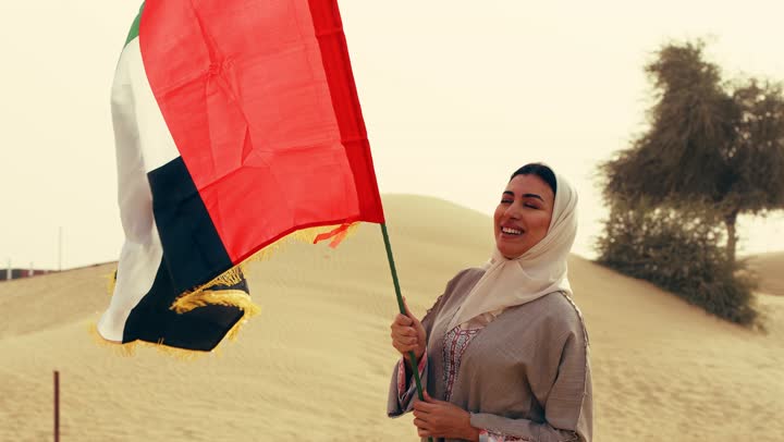 اليوم الوطني الاماراتي 1971، يوم العلم 3 نوفمبر, لامراة عربية خليجية اماراتية ترتدي العباءة والحجاب ترفع علم الإمارات في الصحراء, مفهوم حب الوطن والانتماء اليه, إحياء ذكرى استقلال دولة الإمارات العربية المتحدة, ذكرى تأسيس الاتحاد 2 ديسمبر