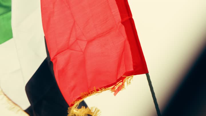 تصوير مقرب لامراة عربية خليجية اماراتية ترتدي العباءة والحجاب ترفع علم الإمارات في الصحراء, مفهوم حب الوطن والانتماء اليه, إحياء ذكرى استقلال دولة الإمارات العربية المتحدة, ذكرى تأسيس الاتحاد 2 ديسمبر