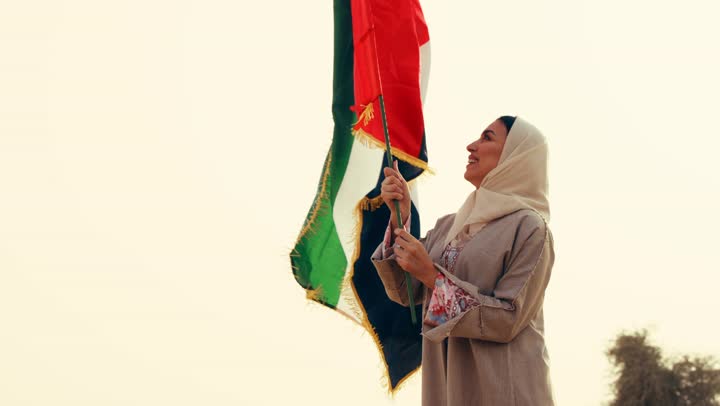 ذكرى تأسيس الاتحاد 2 ديسمبر, امراة عربية خليجية اماراتية ترتدي العباءة والحجاب ترفع علم الإمارات في الصحراء, مفهوم حب الوطن والانتماء اليه, إحياء ذكرى استقلال دولة الإمارات العربية المتحدة