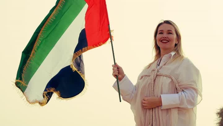 إمراة عربية خليجية إماراتية ترتدي العباءة تمسك بيدها علم الإمارات العربية المتحدة تقف في الصحراء، يوم العلم 3 نوفمبر، حب الوطن والاعتزاز به, استذكار اليوم الوطني الاماراتي 1971,  ذكرى تأسيس الاتحاد 2 ديسمبر