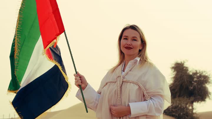 ذكرى تأسيس الاتحاد 2 ديسمبر، إمراة عربية خليجية إماراتية ترتدي العباءة تمسك بيدها علم الإمارات العربية المتحدة تقف في الصحراء، يوم العلم 3 نوفمبر، حب الوطن والاعتزاز به, استذكار اليوم الوطني الاماراتي 1971