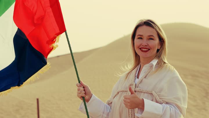 استذكار اليوم الوطني الاماراتي 1971، ذكرى تأسيس الاتحاد 2 ديسمبر، إمراة عربية خليجية إماراتية ترتدي العباءة تمسك بيدها علم الإمارات العربية المتحدة تقف في الصحراء، يوم العلم 3 نوفمبر، حب الوطن والاعتزاز به