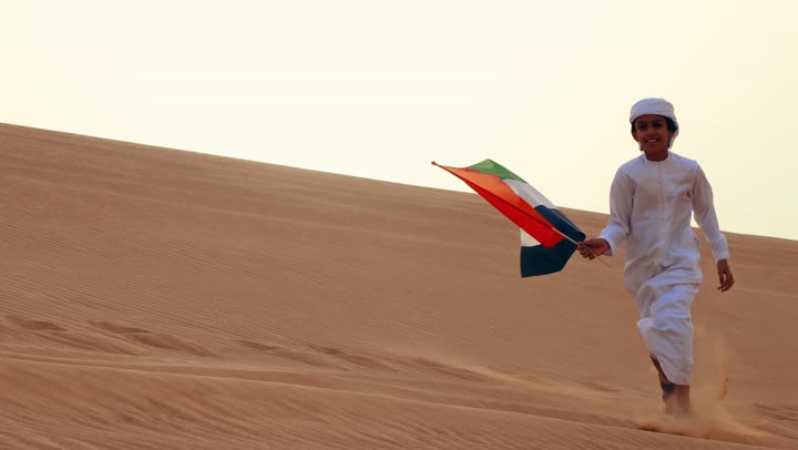 علم وراية الوطن, طفل عربي خليجي إماراتي يرتدي الكندورة و الغترة البيضاء يمسك بيده علم الإمارات العربية المتحدة يركض في الصحراء, حب الوطن والاعتزاز به, استذكار اليوم الوطني الاماراتي 1971