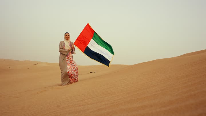 إحياء ذكرى استقلال دولة الإمارات العربية المتحدة, امراة عربية خليجية اماراتية ترتدي العباءة والحجاب ترفع علم الإمارات في الصحراء, مفهوم حب الوطن والانتماء اليه, الاحتفال باليوم الوطني الإماراتي 2 ديسمبر