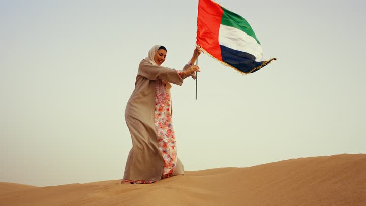 امراة عربية خليجية اماراتية ترتدي العباءة والحجاب ترفع علم الإمارات في الصحراء, مفهوم حب الوطن والانتماء اليه, الاحتفال باليوم الوطني الإماراتي 2 ديسمبر، إحياء ذكرى استقلال دولة الإمارات العربية المتحدة