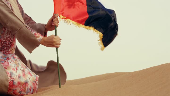 The celebration of the UAE National Day on December 2, commemorating the independence of the United Arab Emirates, an Arab Gulf Emirati woman wearing an abaya and hijab raises the UAE flag in the desert, the concept of love for the homeland and belonging to it.