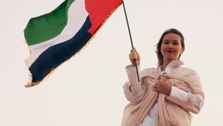 Celebrating the UAE National Day on December 2, commemorating the independence of the United Arab Emirates, an Arab Gulf Emirati woman wearing an abaya stands in the desert, gestures of happiness, pride, and honor, the concept of love for the homeland and belonging to it.