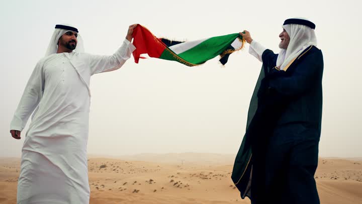 رجلان عربيان خليجيان اماراتيان يرتديان الزي التقليدي يرفعان علم الامارات العربية المتحدة في الصحراء، ارتداء الازياء الشعبية التقليدية للاحتفال بذكرى تأسيس الاتحاد 2 ديسمبر، يوم العلم 3 نوفمبر, حب الوطن والاعتزاز به