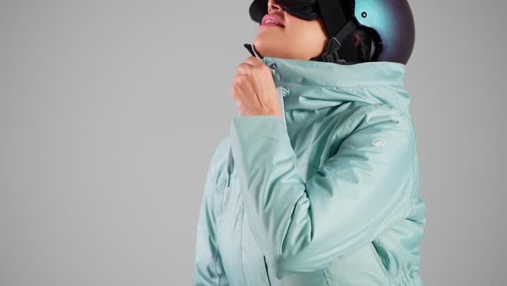 Zipping up the blue coat for protection against the cold, an Arab Gulf Saudi woman is wearing ski clothes and a helmet, an Emirati woman.