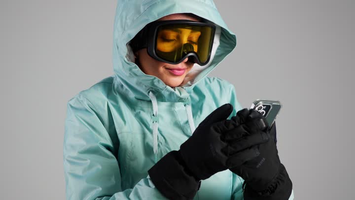 Difficulty using a mobile phone while wearing heavy gloves, a Gulf Arab Saudi woman wearing ski clothing, an Emirati woman, gestures of discomfort.