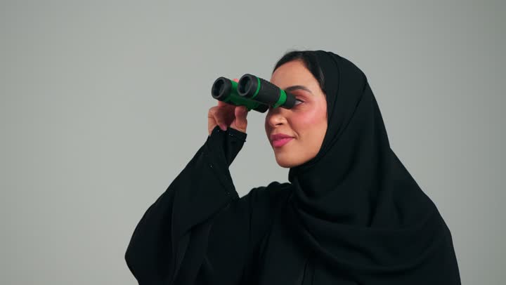 النظر للاعلى لشئ ما متحرك , ارمرأة عربية خليجية سعودية محجبة ترتدي العباءة السوداء تحمل المنظار المقرب , ايماءات المفاجأة و الدهشة , امرأة اماراتية , رفع اصبع السبابة للاشارة الى شئ بعيد