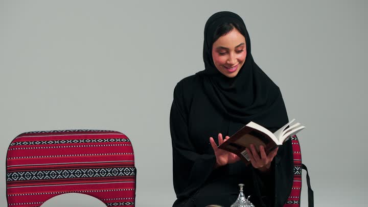 التقليب في صفحات الكتاب المميز , امرأة عربية سعودية خليجية محجبة ترتدي العباءة السوداء تقوم بالقراءة المفيدة اثناء الاستمتاع بالاجواء الشتوية , الشعور بالسكينة و السعادة , امراة اماراتية
