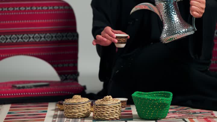 تصوير مقرب للنزهة الشتوية الممتعة , امرأة عربية خليجية سعودية محجبة ترتدي العباءة السوداء تملأ كوب القهوة من الابريق الفضي , لحظات من الاسترخاء و الراحة , امراة اماراتية