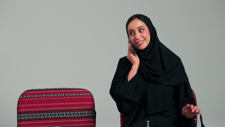 التواصل مع الاصدقاء بسهولة من اي مكان , امراة عربية خليجية سعودية محجبة ترتدي عباءة سوداء تتحدث بالهاتف المحمول , ايماءات السعادة اثناء استقبال المكالمات , امرأة اماراتية
