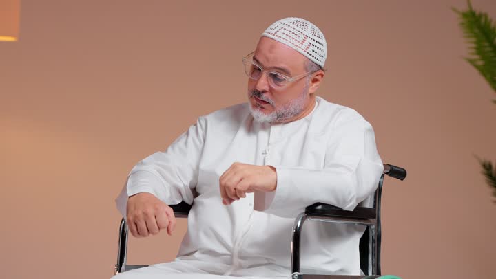 An elderly Saudi Arabian Gulf man wearing a white thobe and a white ghutrah is sitting in a wheelchair, while a doctor is measuring his body temperature, checking on his health, with expressions of concern and fear.