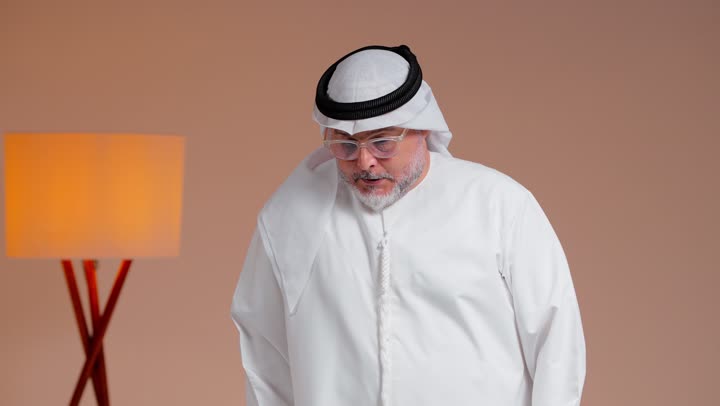 رفع اصبع الابهام لاعلى علامة على الاعجاب و الموافقة , رجل عربي خليجي سعودي مسن يرتدة الغترة البيضاء و الثوب الابيض يستخدم العكاز الخشبي في المشي , ايماءات السعادة و الابتسامة امام الكاميرا