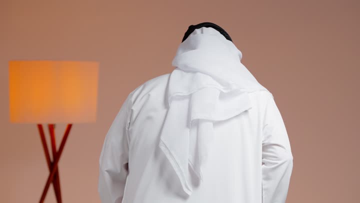 الاستناد على العكاز الخشبي و الحركة البطيئة في المشي , رجل عربي خليجي سعودي مسن يرتدي الثوب الابيض والغترة البيضاء , تصوير من الخلف ,