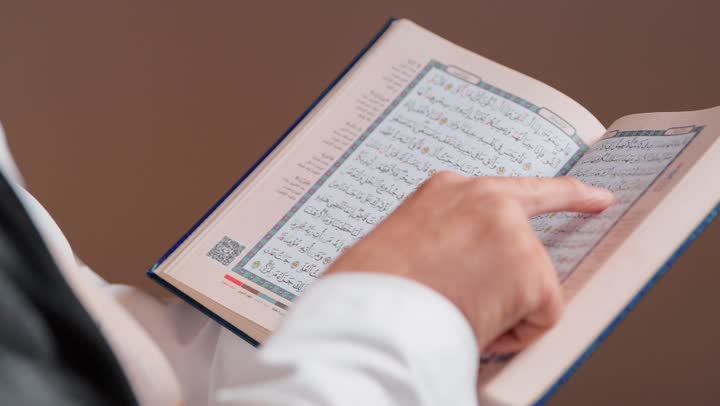 Pointing with the index finger to the words of the Most Merciful, an elderly Arab Gulf Saudi man wearing a traditional white thobe in the Kingdom of Saudi Arabia, reading what is easy from the verses of the Holy Quran, feeling tranquility and peace.