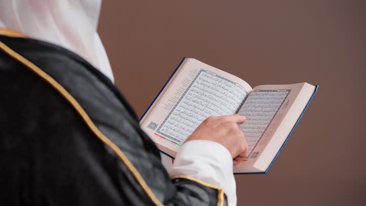 قراءة ايات الذكر الحكيم , مسن عربي خليجي سعودي يرتدي الثوب التقليدي الابيض في المملكة , الغترة البيضاء و المشلح الاسود الانيق , لمس صفحات المصحف الشريف باصبع السبابة