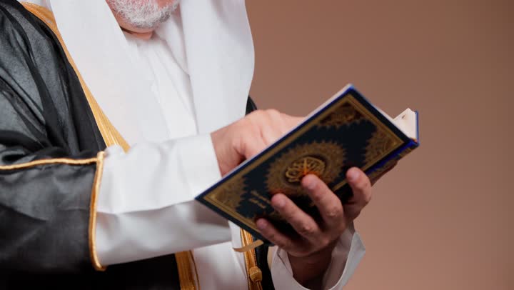 القراءة السهلة الميسرة في الكتاب الشريف , رجل عربي خليجي سعودي مسن يرتدي البشت الاسود و الغترة البيضاء و الثوب الابيض التقليدي في المملكة يحمل المصحف الكريم , الشعور بالسلام و السكينة , لمس المصحف و تتبع الكلمات باصبع السبابة