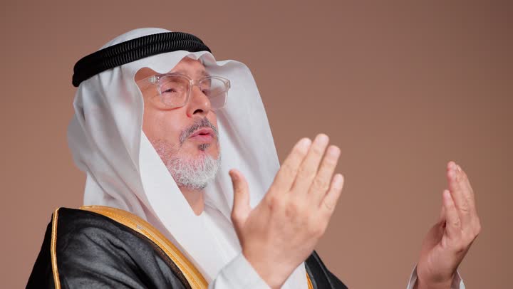 Raising hands to the sky and praying, an elderly Arab Gulf Saudi man wearing a white thobe and a black bisht is drawing closer to God with hope.