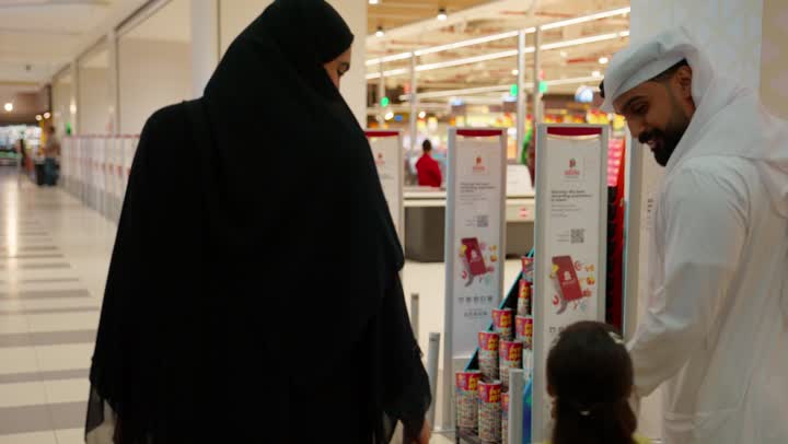 Preparing to buy household needs, the concept of family shopping, spending family time and strolling inside the mall, a rear view of an Emirati Gulf Arab family wearing traditional attire inside a shopping center, a father wearing a kandura and ghutrah walking with his wife and their daughter, family communication and bonding.