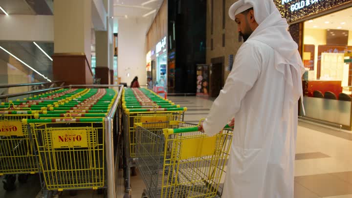 قضاء وقت عائلي أثناء التسوق وشراء الاحتياجات المنزلية، عائلة عربية خليجية إماراتية ترتدي الزي التقليدي داخل السوبر ماركت، رجل يرتدي الكندورة والغترة يدفع عربة التسوق برفقة زوجته وابنتهما ، مفهوم التسوق الأسري، ايماءات السعادة و السرور