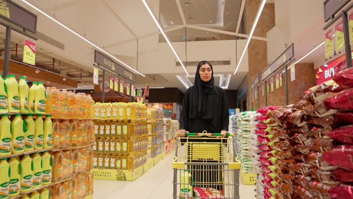 امرأة عربية خليجية إماراتية محجبة ترتدي العباءة تقوم بدفع عربة التسوق داخل السوبر ماركت وشراء المواد الغذائية والتموينية، مفهوم التسوق اليومي، اختيار الاحتياجات المنزلية، شراء الأرز والبقالة