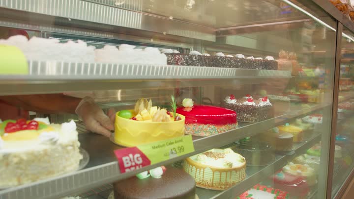 ايماءات السعادة والسرور، مفهوم التسوق العائلي وشراء الحلويات، رجل عربي خليجي اماراتي يرتدي الكندورة و الغترة يحمل قطعة كيك ويقدمه لابنتة داخل السوبرماركت