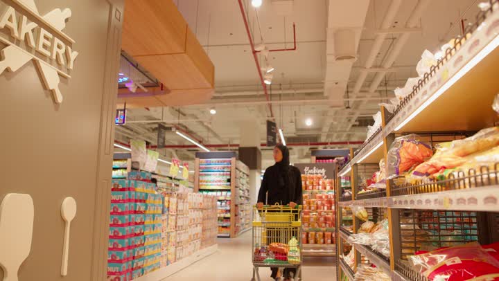 مفهوم التسوق وشراء المخبوزات والمعجنات، امرأة عربية خليجيه اماراتية ترتدي العباءة والحجاب تجر عربة التسوق داخل السوبر ماركت، التسوق اليومي داخل المتجر، الاستفادة من العروض والتخفيضات