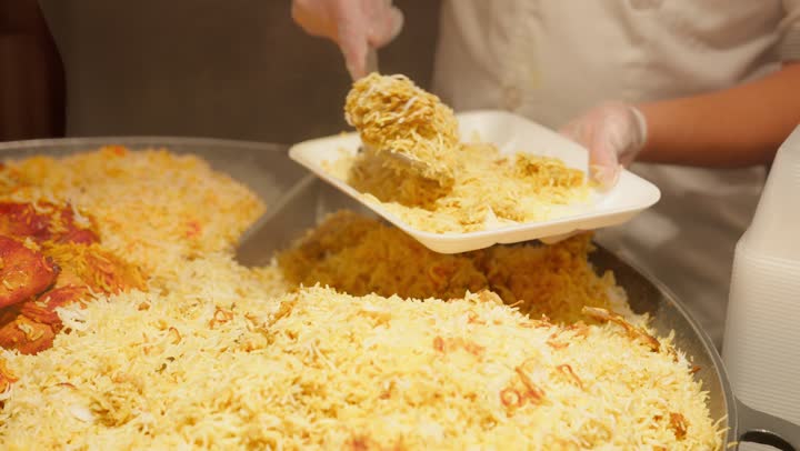 أطعمة عربية شعبية، مفهوم شراء الطعام الجاهز، وجبات ساخنة جاهزة للأكل داخل قسم الديلي، تصوير مقرب لعامل عربي خليجي اماراتي داخل قسم الأطعمة الجاهزة في السوبر ماركت  يقوم بتقديم وجبة أرز مع دجاج باستخدام ملعقة تقديم، خدمة العملاء داخل المتجر