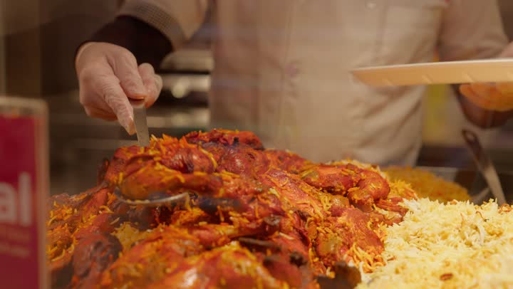 مفهوم شراء الطعام الجاهز، وجبات ساخنة جاهزة للأكل داخل قسم الديلي، تصوير مقرب لعامل عربي خليجي اماراتي داخل قسم الأطعمة الجاهزة في السوبر ماركت  يقوم بتقديم وجبة أرز مع دجاج باستخدام ملعقة تقديم، أطعمة عربية شعبية، خدمة العملاء داخل المتجر