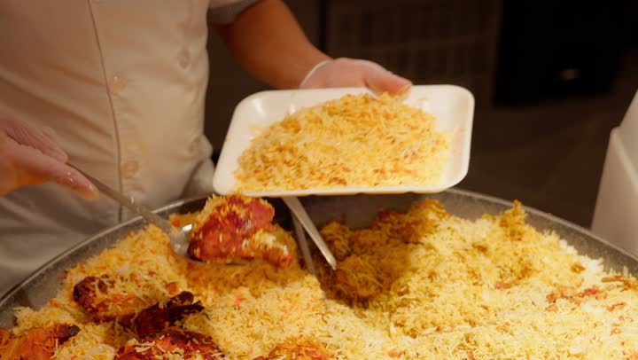 Hot ready-to-eat meals in the deli section, a close-up shot of an Emirati Gulf Arab worker in the ready-to-eat food section of the supermarket serving a rice and chicken meal using a serving spoon, the concept of buying ready-made food, popular Arab foods, customer service inside the store.