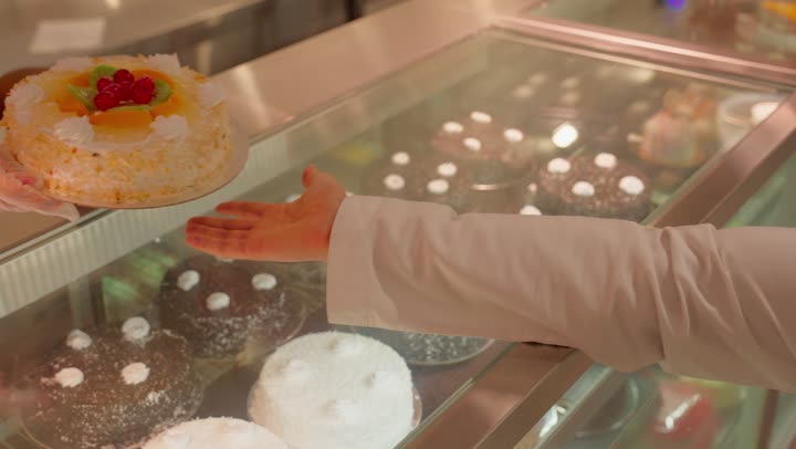 مفهوم شراء الحلويات والكيك، تصوير مقرب ليد رجل عربي خليجي اماراتي يقوم باستلام كعكة مزينة بالفواكه الطازجة من داخل ثلاجة العرض، منتجات مخبوزة طازجة