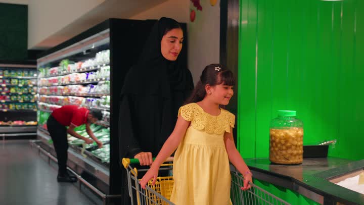 بنت عربية خليجية اماراتية ترتدي الفستان تقوم باختيار عبوة عصير من قسم المشروبات داخل المتجر برفقة والدتها، مفهوم التسوق العائلي وتعليم الأطفال اختيار المنتجات، قضاء وقت ممتع داخل السوبر ماركت، الاهتمام بالتغذية الصحية واختيار المشروبات المناسبة