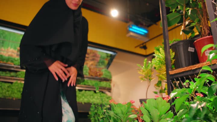 نمط حياة صحي وحب الطبيعة، امرأة عربية خليجية اماراتية ترتدي العباءة والحجاب تقوم باختيار نباتات الزينة داخل السوبر ماركت برفقة ابنتها و زوجها، شراء شتلات خضراء للديكور المنزلي، مفهوم العناية بالنباتات والاهتمام بالبيئة الخضراء، التسوق وشراء مستلزمات المنزل