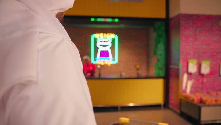 مفهوم شراء الاحتياجات اليومية، التسوق داخل السوبر ماركت، تصوير من الخلف لعائلة عربية خليجية اماراتية ترتدي الزي التقليدي تقوم بوزن الفواكه والخضروات الطازجة في قسم المنتجات، موظفة المتجر تساعد العملاء، التسوق العائلي والاستمتاع بوقت داخل المتجر