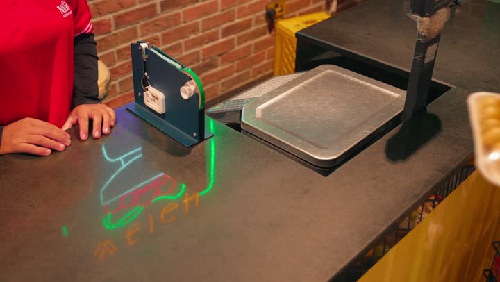 The concept of shopping and buying daily necessities, buying fresh fruits inside the supermarket, a close-up shot of the hand of an Emirati Gulf Arab woman holding a pack of red grapes and a pack of fresh fruit as she pays for her purchases at the cashier, the accounting employee is registering the products on the electronic scale.