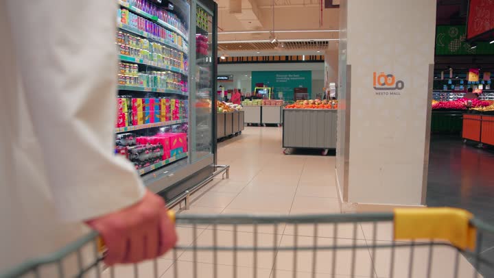 Conscious shopping and choosing the right products, buying daily household needs, a close-up shot of the hand of an Arab Gulf Emirati man pushing a shopping cart down the aisle of consumer products in the supermarket.