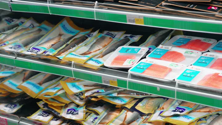 مفهوم التغذية الصحية، تجهيز وجبات بحرية منزلية، تصوير مقرب ليد رجل عربي خليجي اماراتي يرتدي الزي التقليدي يختار عبوة مأكولات متبلة من ثلاجة قسم الأسماك في السوبر ماركت